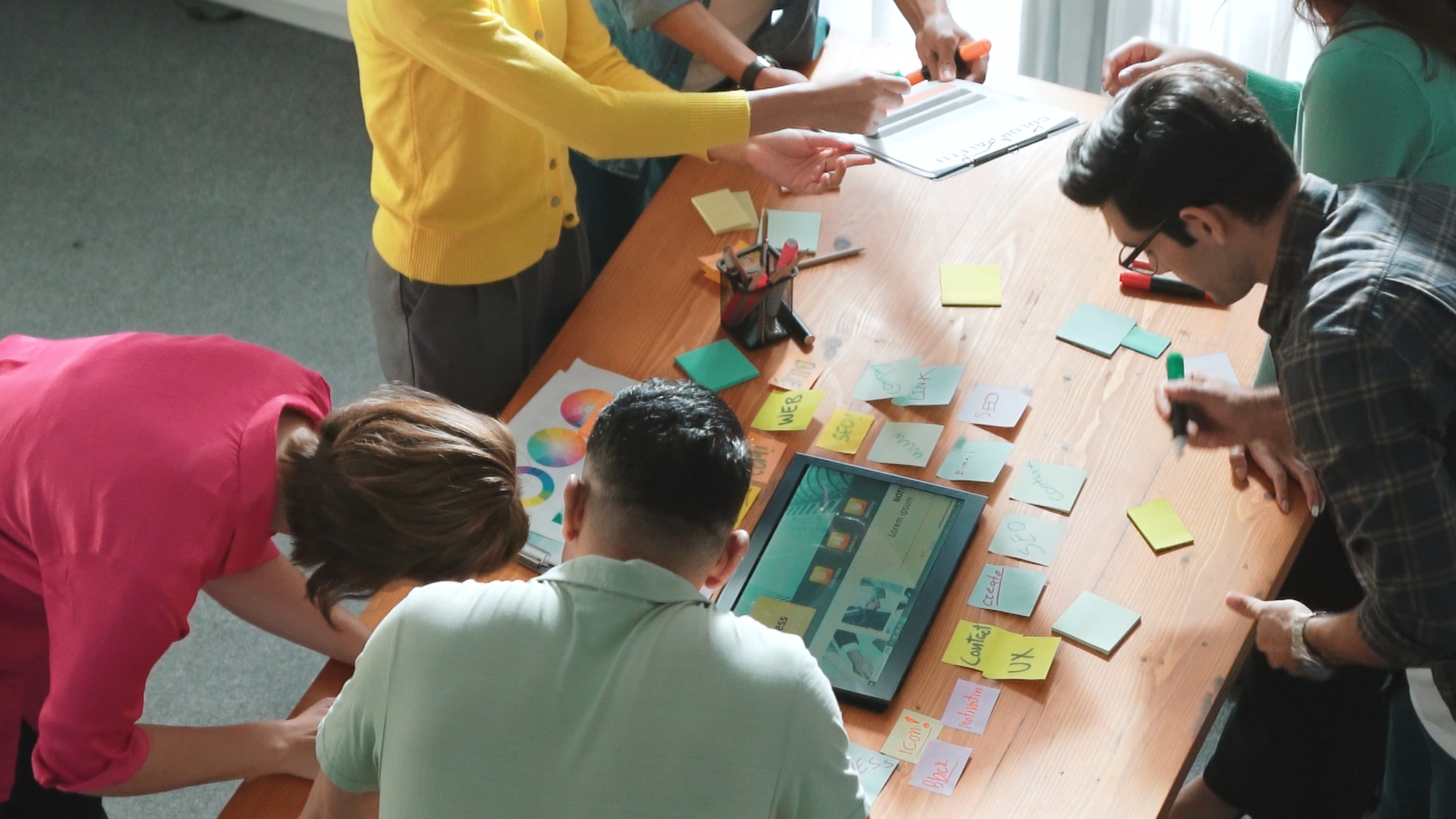 Personas reunidas alrededor de una mesa trabajando con notas adhesivas, gráficos y una tablet durante una sesión de planificación en equipo.