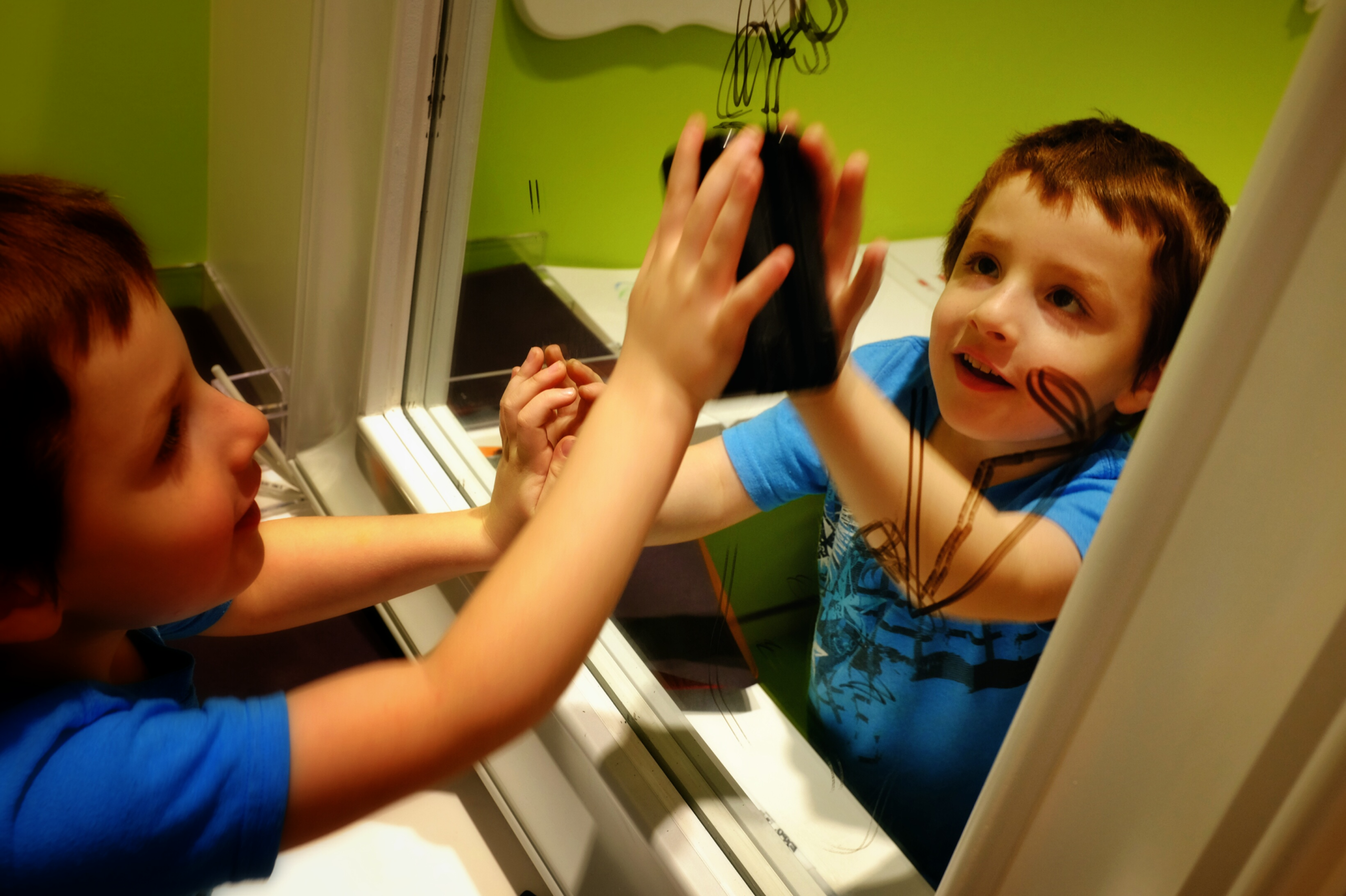 Niño jugando frente a un espejo, observando su reflejo y sonriendo mientras sostiene un objeto con curiosidad.