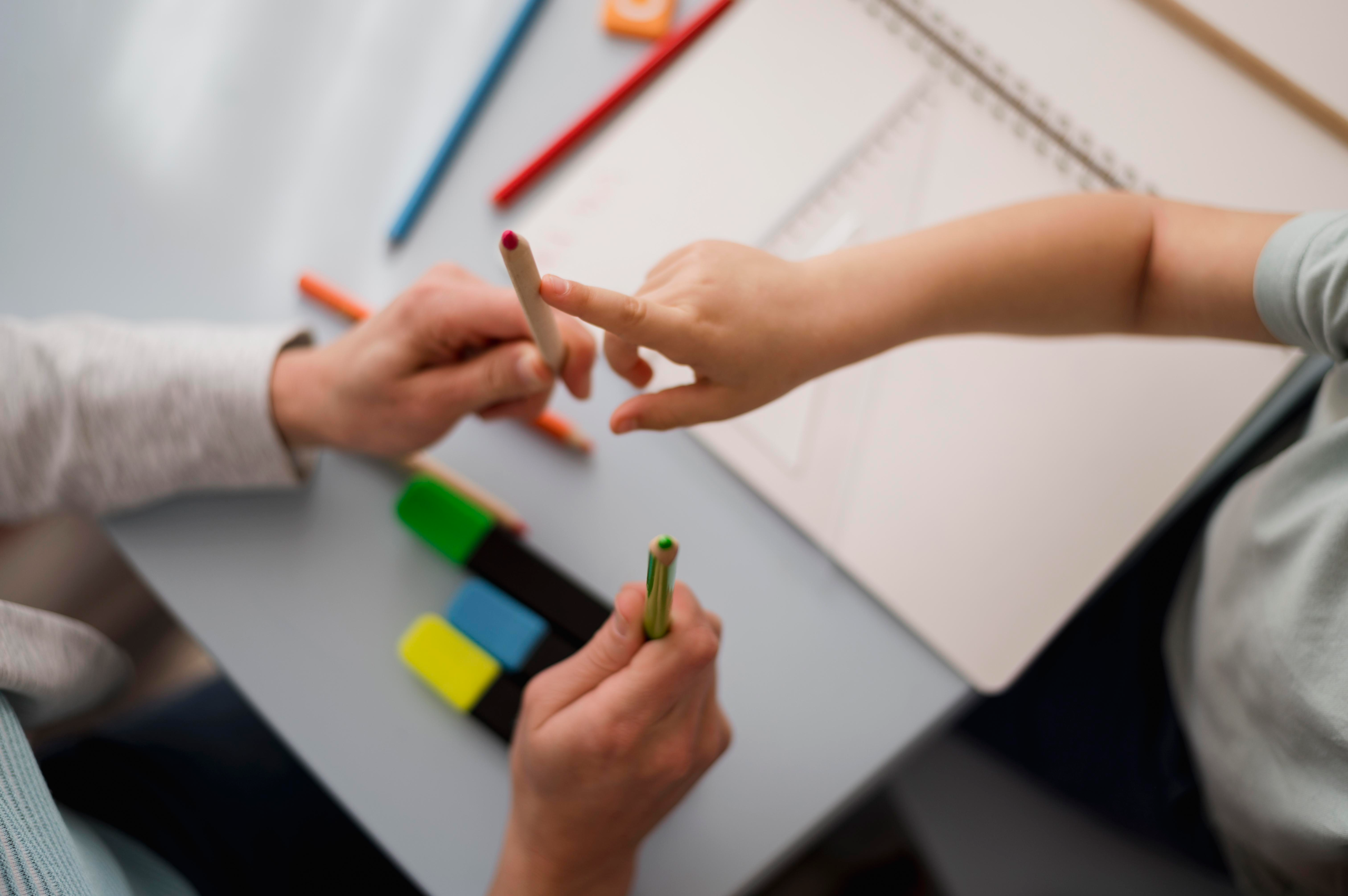Niño aprendiendo a contar junto a un adulto, con lápices de colores y cuaderno sobre una mesa.